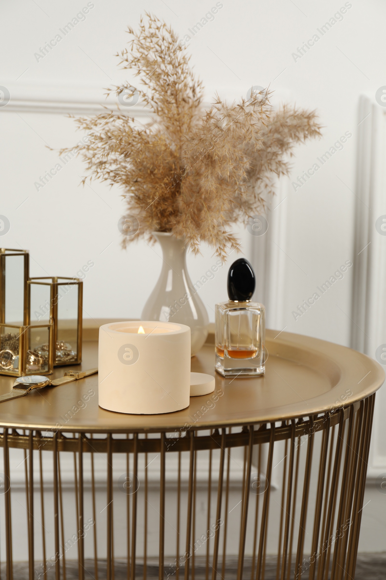 Photo of Burning soy candle, perfume and stylish accessories on table indoors