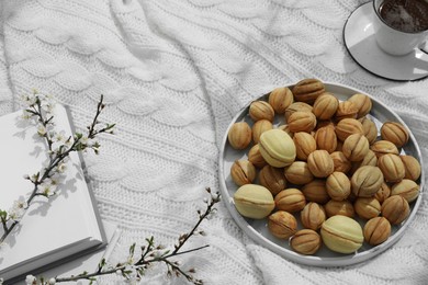 Delicious walnut shaped cookies with filling, cherry branches, notebook and cup of coffee on white knitted blanket, view from above and space for text. Homemade popular biscuits from childhood