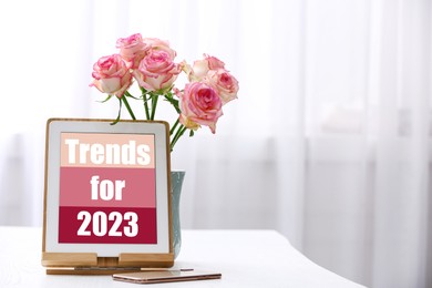 Image of Trends For 2023 text on tablet display. Device, phone and flowers on white table, space for text