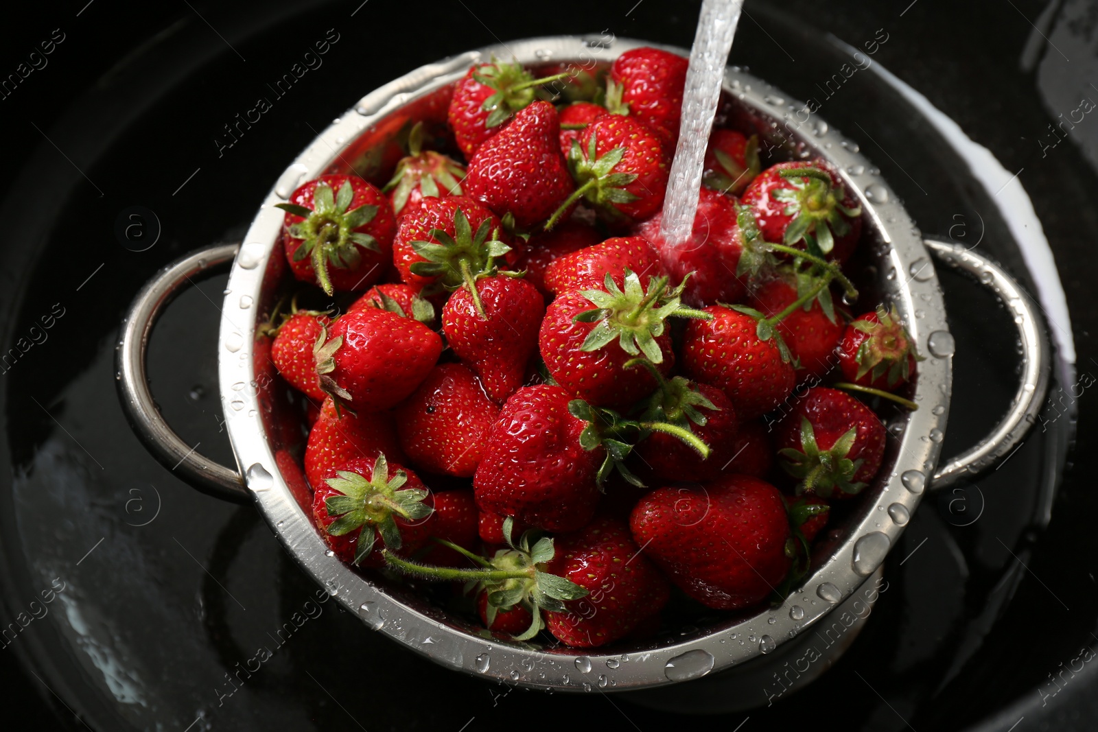 Photo of Washing fresh strawberries under tap water in metal colander in sink, top view