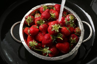 Washing fresh strawberries under tap water in metal colander in sink, top view