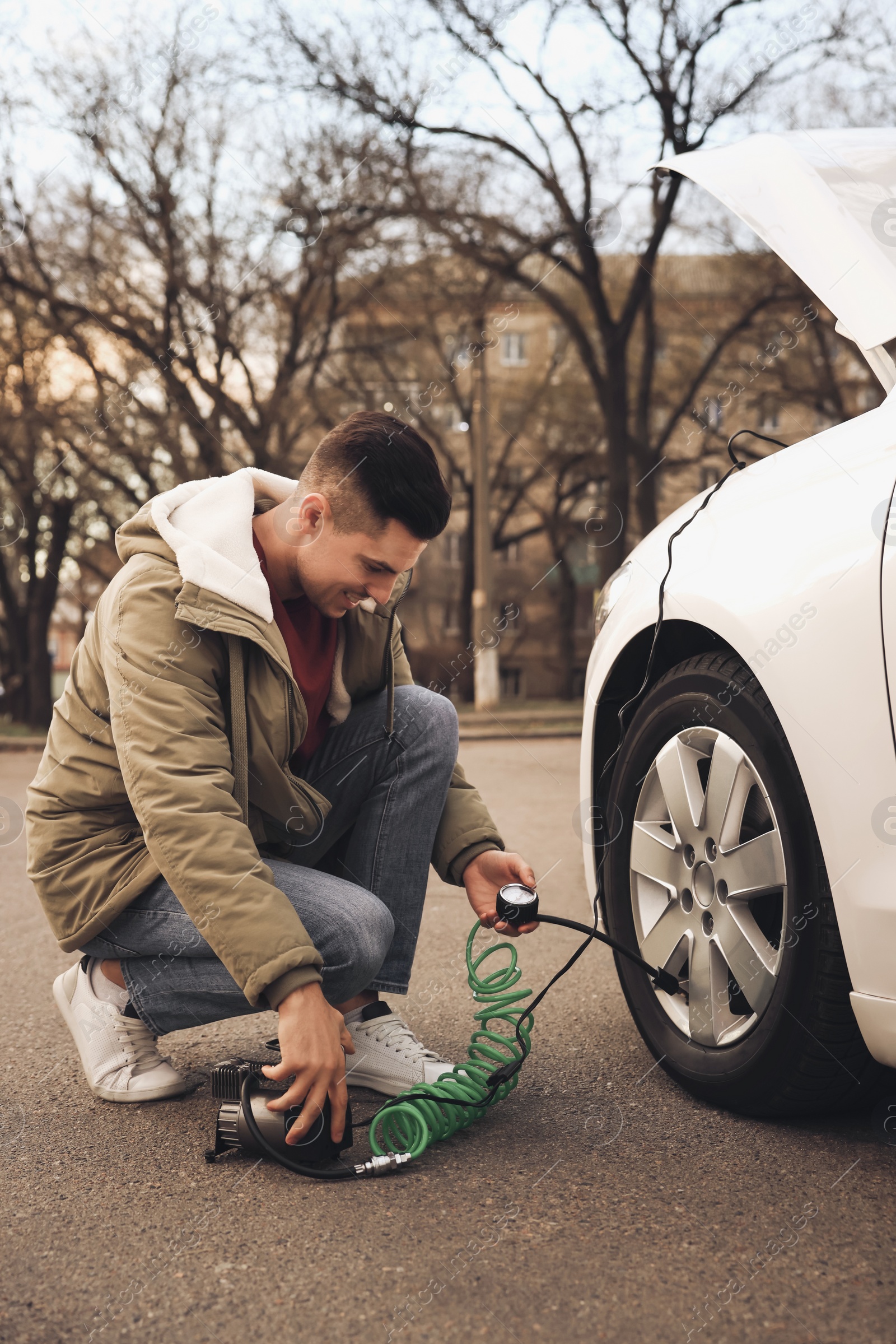 Photo of Handsome man inflating car tire with air compressor on street