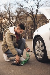 Handsome man inflating car tire with air compressor on street