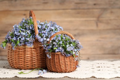 Beautiful forget-me-not flowers in wicker baskets on wooden table, closeup. Space for text