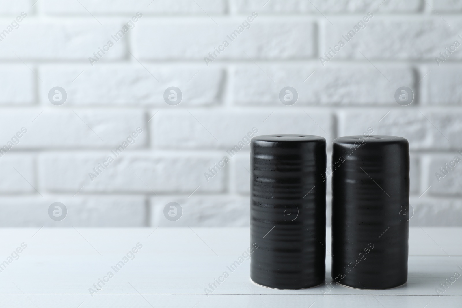 Photo of Salt and pepper shakers on white wooden table. Space for text