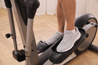 Man using modern elliptical machine indoors, closeup