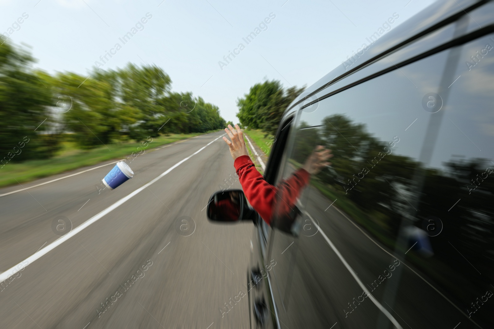 Photo of Driver throwing away paper coffee cup from car window. Garbage on road