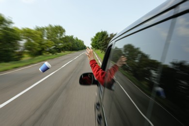 Photo of Driver throwing away paper coffee cup from car window. Garbage on road