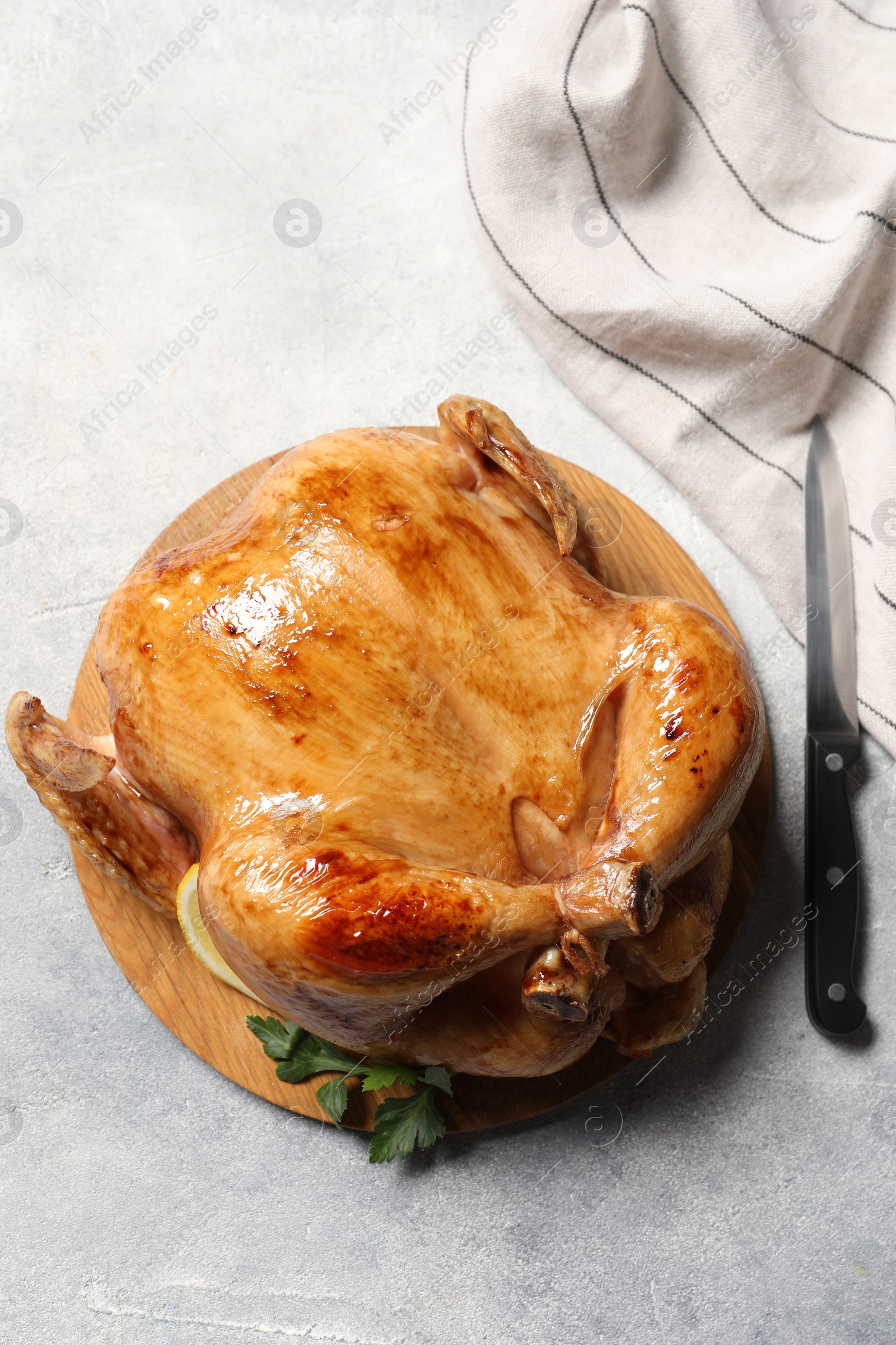 Photo of Tasty roasted chicken with parsley and knife on light grey table, flat lay