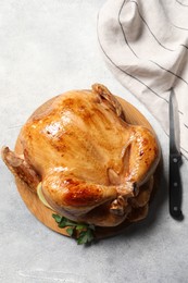 Tasty roasted chicken with parsley and knife on light grey table, flat lay