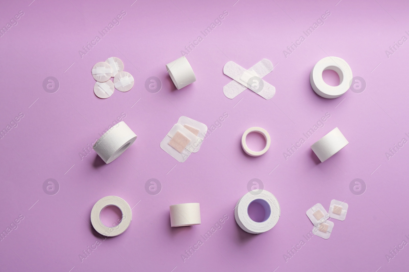 Photo of Different types of sticking plasters on lilac background, flat lay
