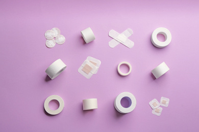 Different types of sticking plasters on lilac background, flat lay