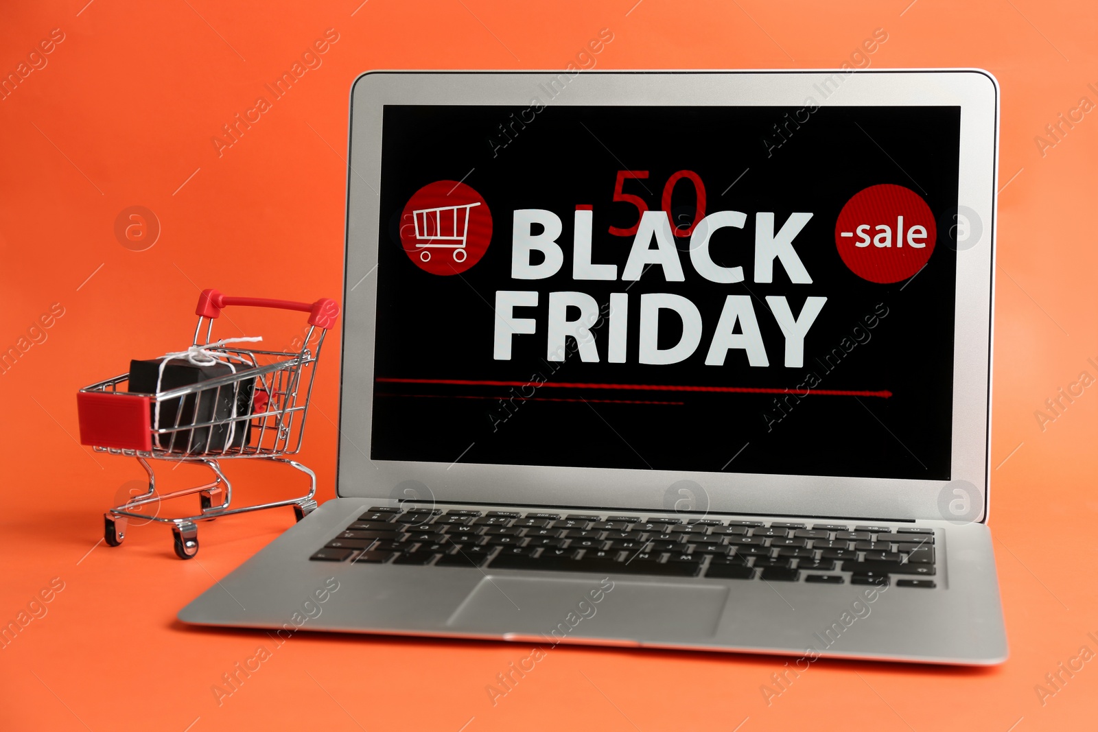 Photo of Laptop with Black Friday announcement, small shopping cart and gift on orange background