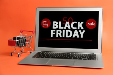 Photo of Laptop with Black Friday announcement, small shopping cart and gift on orange background