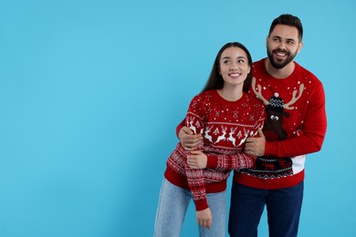 Photo of Happy young couple in Christmas sweaters on light blue background. Space for text