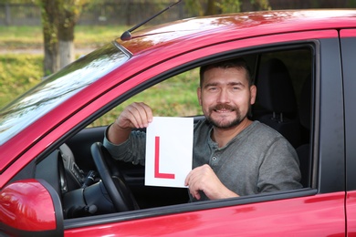 Man showing learner driver sign from new car. Get driving license
