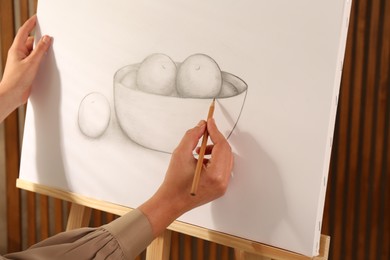 Photo of Woman drawing bowl of fruits with graphite pencil on canvas indoors, closeup