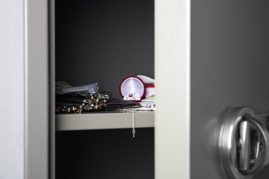 Photo of Open steel safe with money and jewelry, closeup