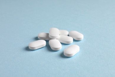 Pile of white pills on light blue background, closeup