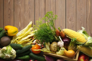 Photo of Different fresh vegetables with crate on wooden table, above view. Farmer harvesting