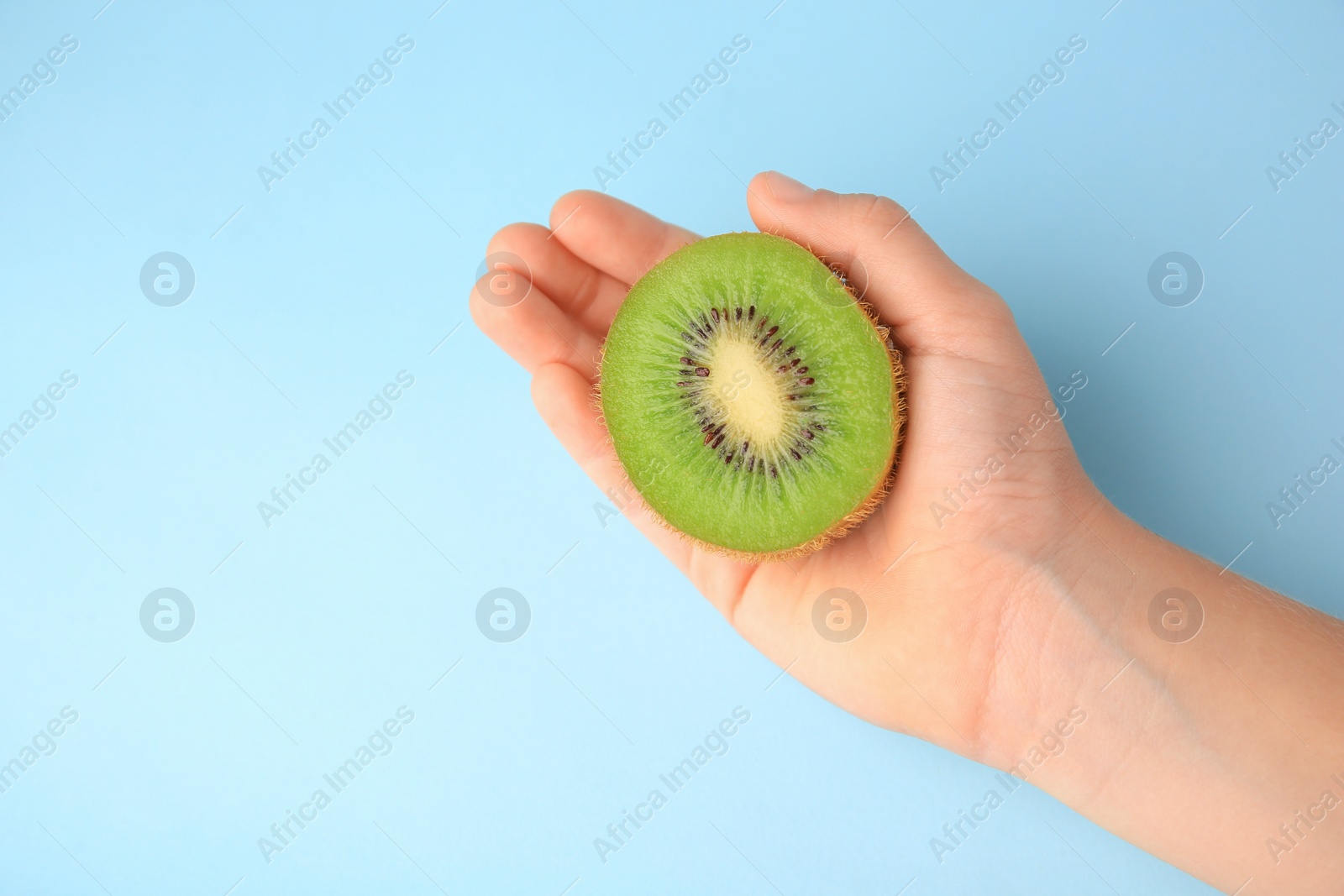 Photo of Woman holding cut fresh kiwi on light blue background, top view. Space for text