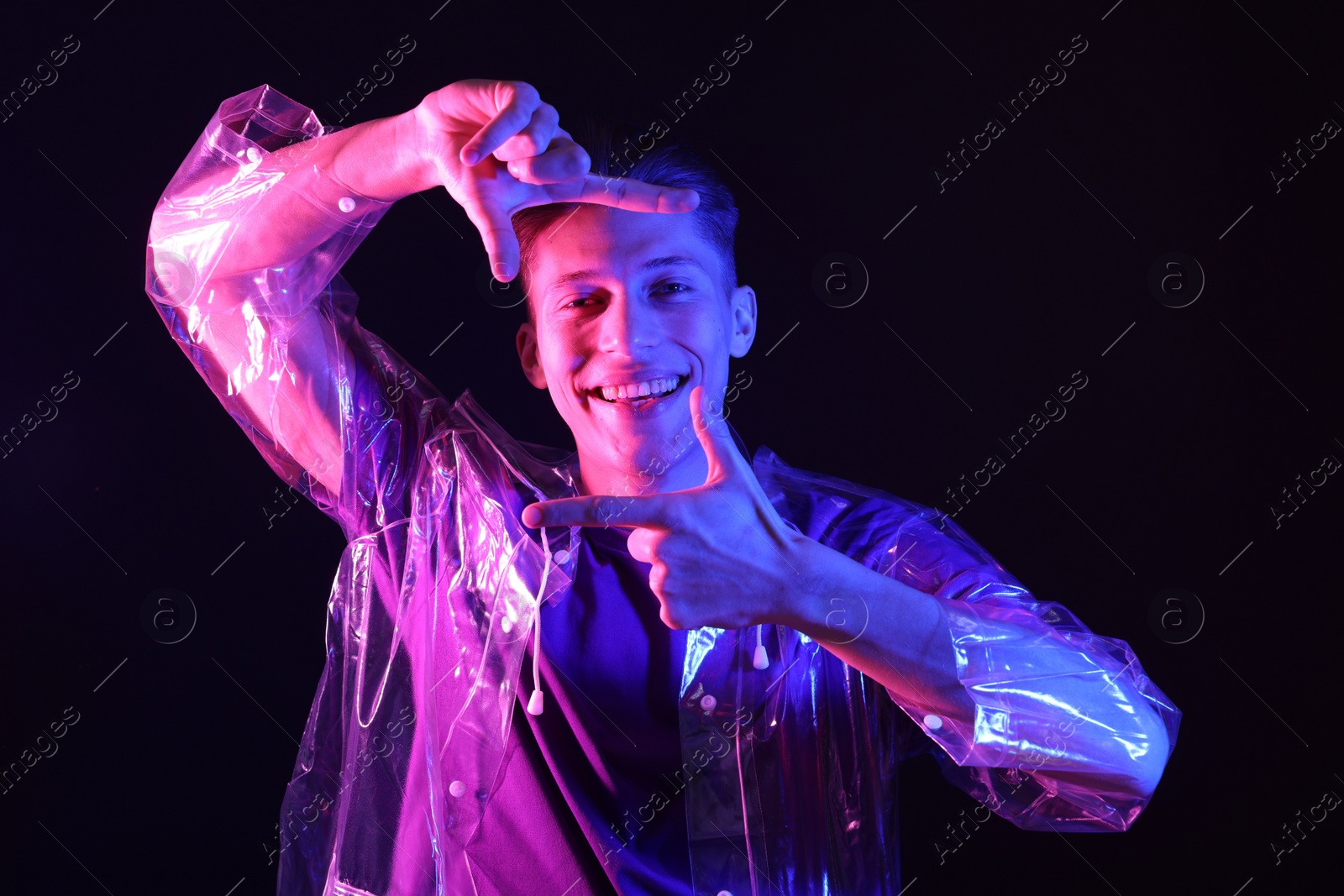 Photo of Young man making camera with hands on dark background in neon lights