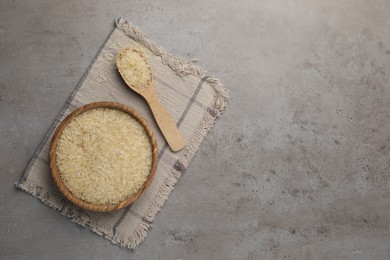Photo of Bowl and spoon of raw rice on grey table, top view. Space for text