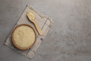 Bowl and spoon of raw rice on grey table, top view. Space for text