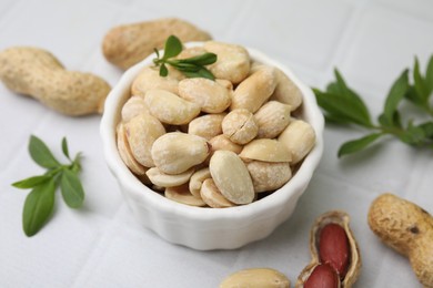 Fresh peeled peanuts in bowl and leaves on white tiled table, closeup