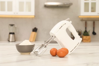 Photo of Modern mixer, eggs and bowl with flour on white marble table in kitchen