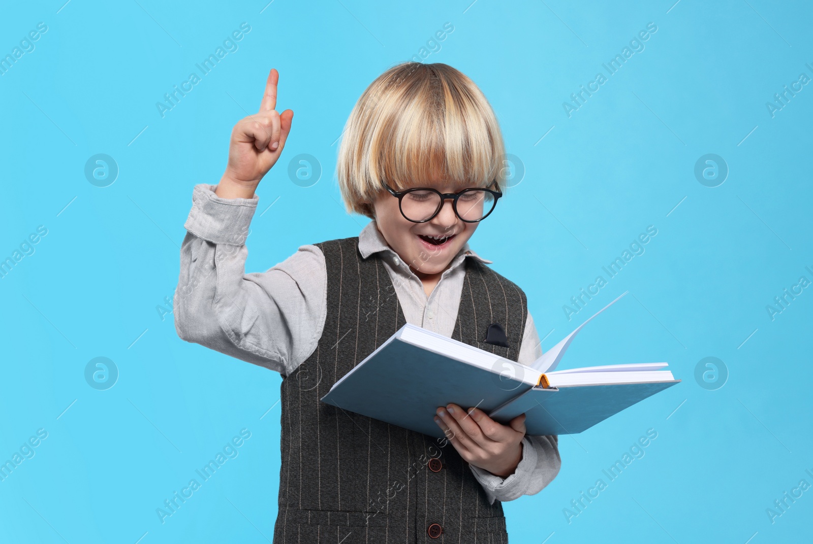 Photo of Cute little boy in glasses reading book on light blue background