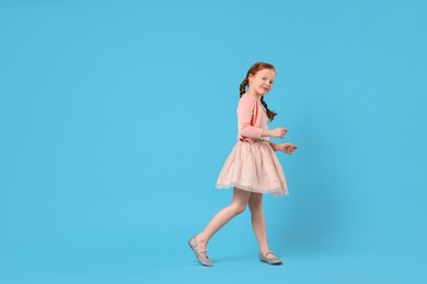 Photo of Cute little girl dancing on light blue background, space for text