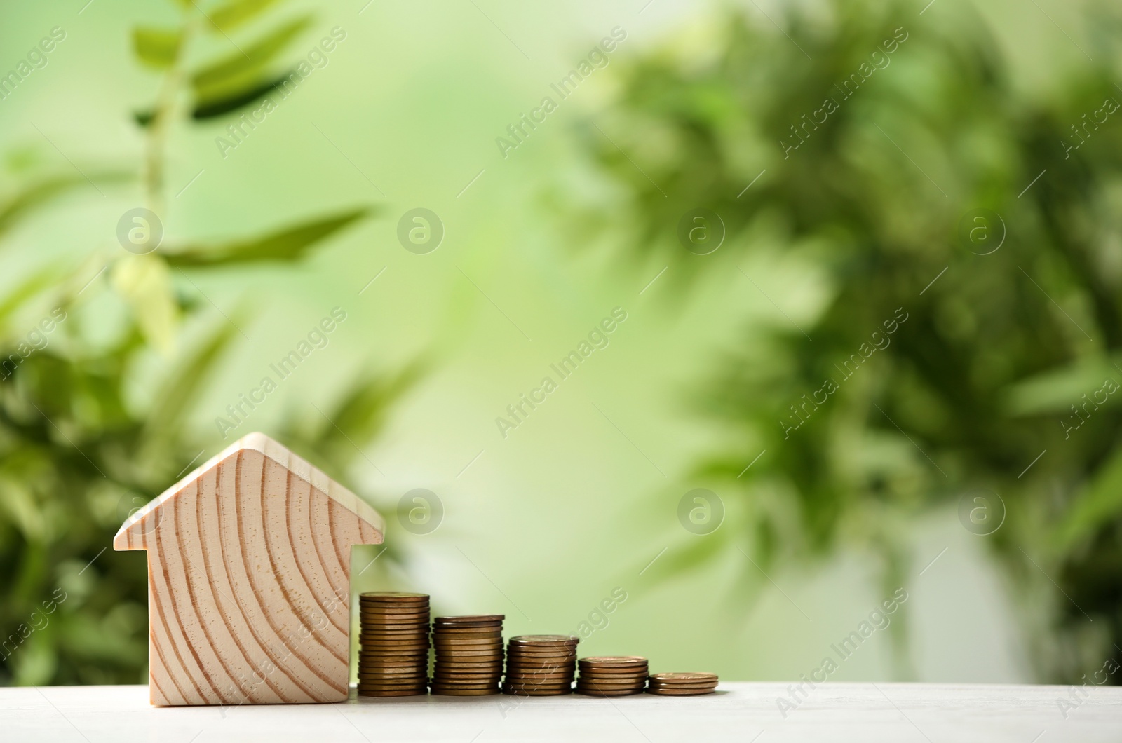 Photo of Model of house and stacked coins on table against blurred green background, space for text