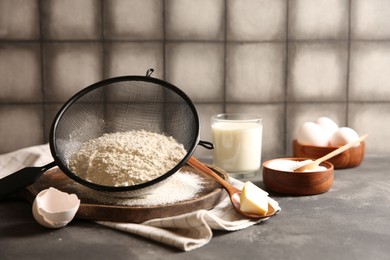 Photo of Making dough. Flour in sieve, spoon and butter on grey table, closeup