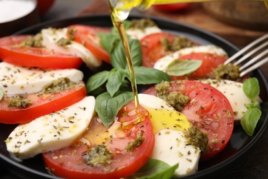 Photo of Pouring olive oil onto delicious Caprese salad with pesto sauce on table, closeup