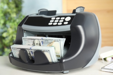 Modern electronic bill counter with money on table indoors, closeup