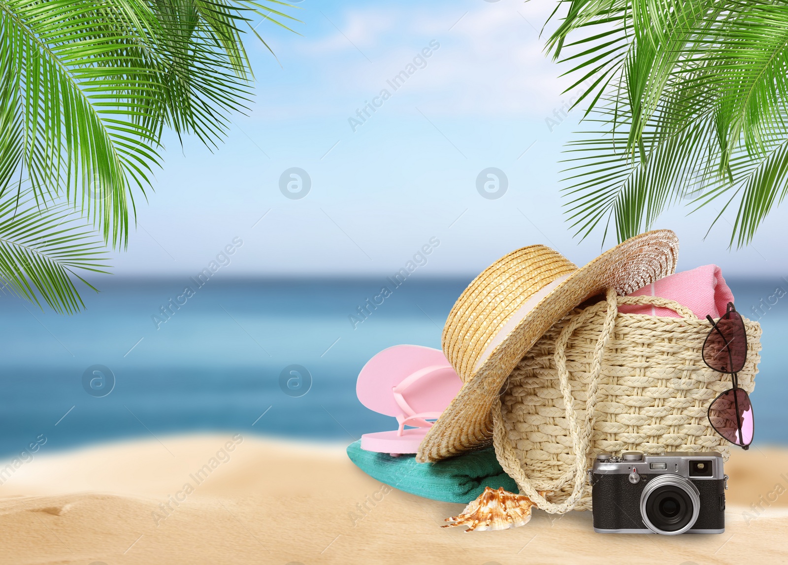 Image of Stylish bag with different accessories on tropical sandy beach, space for text 