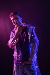 Photo of Young man wearing clear coat in neon lights with smoke effect