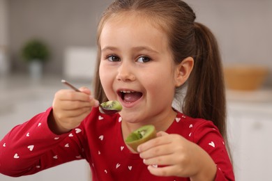 Cute little girl eating fresh kiwi indoors