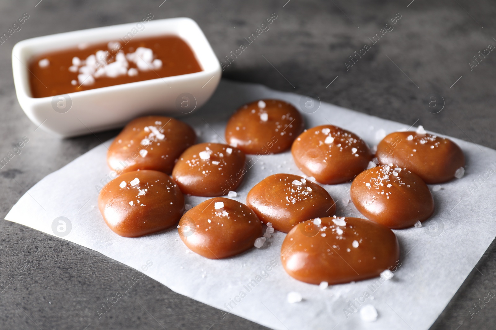 Photo of Tasty candies, caramel sauce and salt on grey table