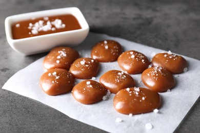 Tasty candies, caramel sauce and salt on grey table