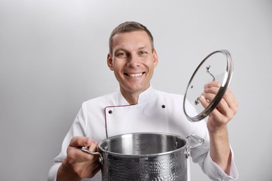 Happy male chef with cooking pot on light grey background