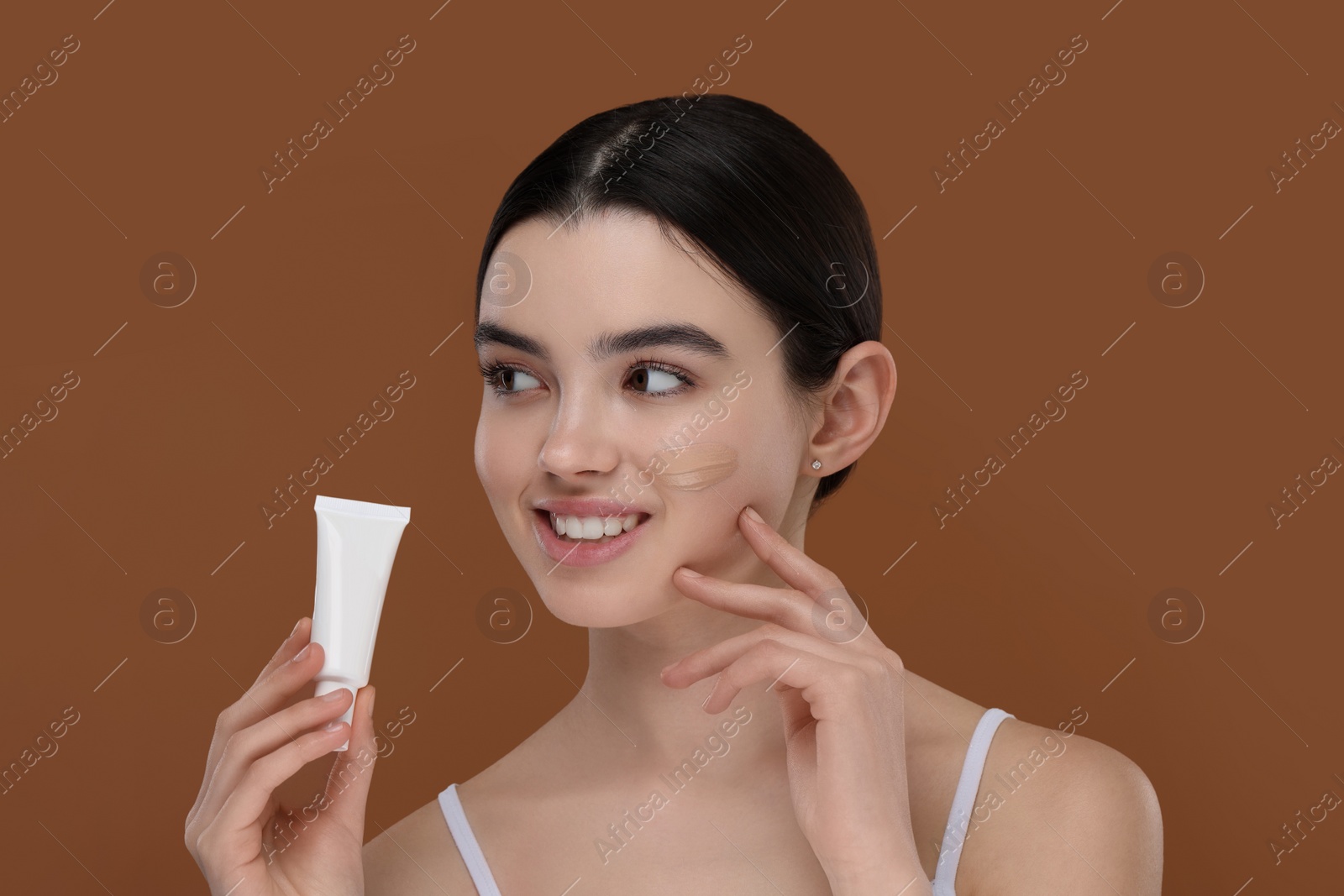 Photo of Teenage girl holding tube with foundation on brown background