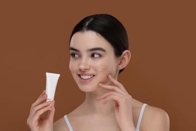 Teenage girl holding tube with foundation on brown background