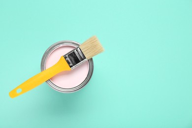 Photo of Can of pink paint with brush on turquoise background, top view. Space for text