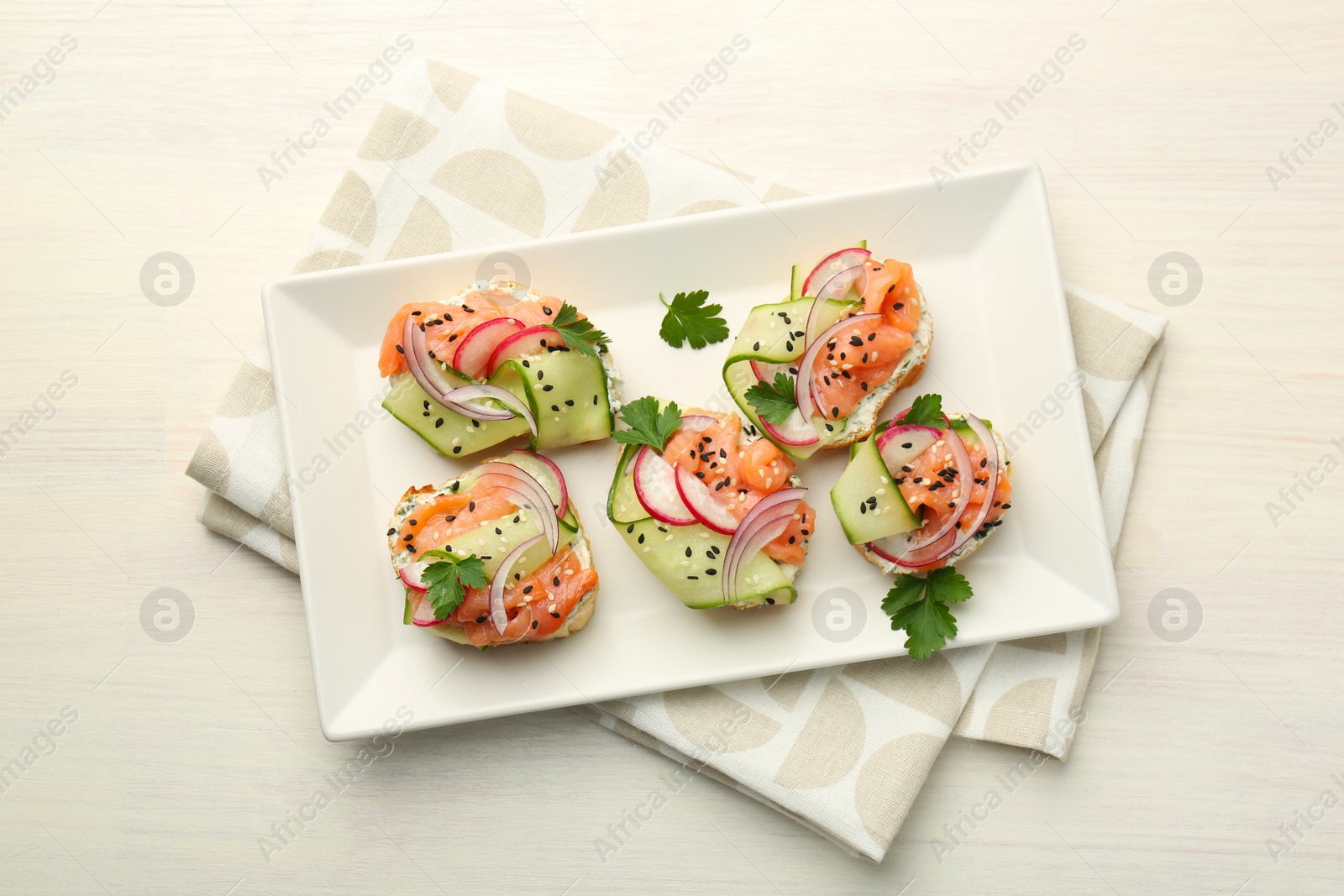 Photo of Tasty canapes with salmon served on white wooden table, top view