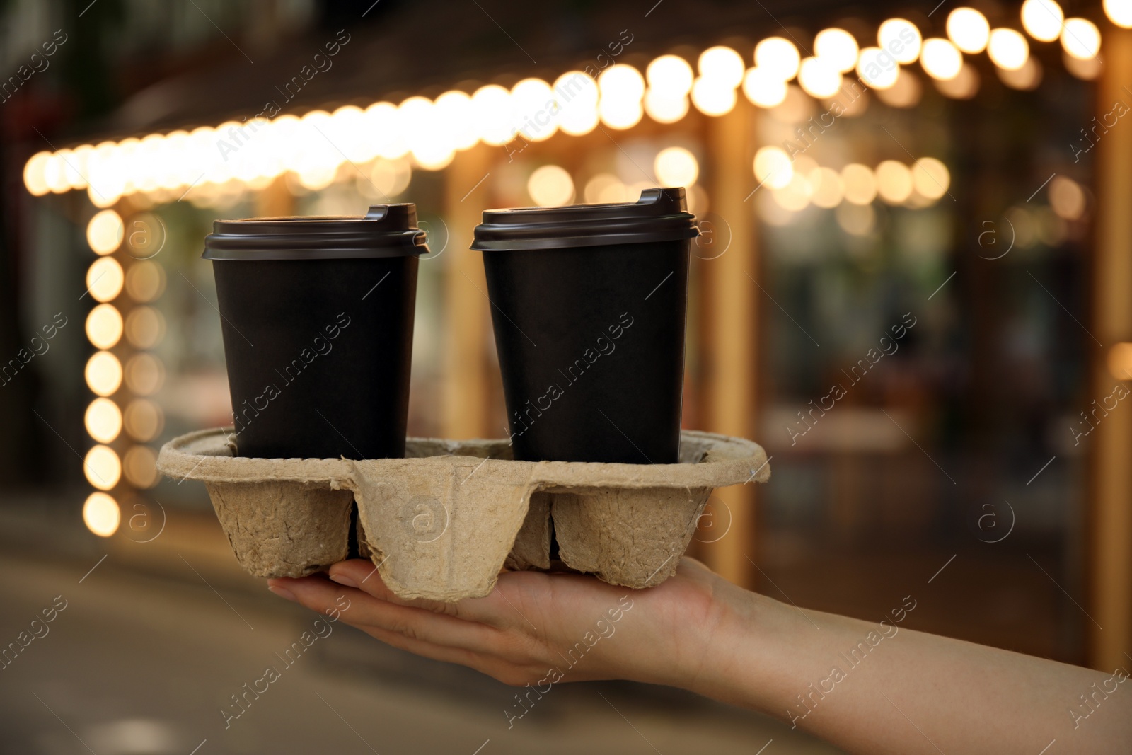 Photo of Woman holding cardboard holder with takeaway paper coffee cups outdoors, closeup