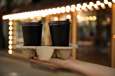 Woman holding cardboard holder with takeaway paper coffee cups outdoors, closeup