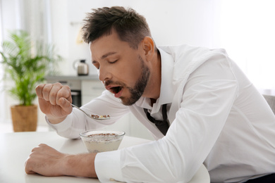 Sleepy man eating breakfast at home in morning