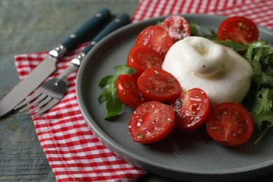 Photo of Delicious burrata cheese with tomatoes and arugula served on grey wooden table, closeup